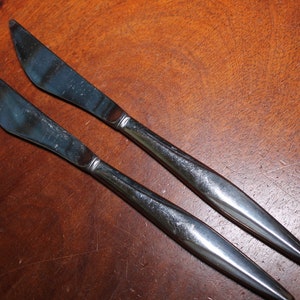 May include: Two silver dinner knives with a modern design. The knives have a pointed tip and a slightly curved handle.