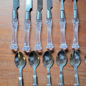 May include: A set of silver cutlery with clear plastic handles. The set includes four butter knives, two forks, and four spoons.