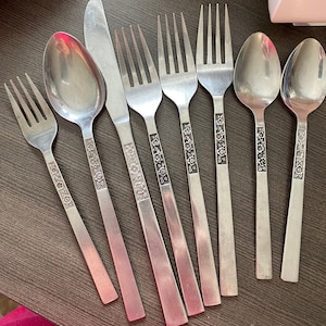May include: A set of nine silver-toned flatware pieces with floral designs. The set includes forks, spoons, and a butter knife.