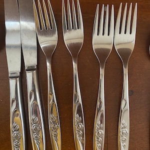 May include: A set of six silver forks and two silver knives with floral designs on the handles.
