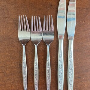 May include: Set of five silver-toned flatware with ornate designs. The set includes three forks and two knives.