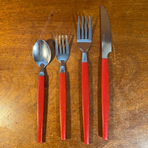 May include: A set of four pieces of silverware: a spoon, two forks, and a knife. The silverware has shiny, silver-colored heads and bright red handles. The knife blade is stainless steel.