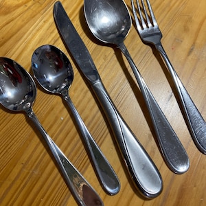 May include: A set of four silver-toned flatware pieces, including a knife, fork, and two spoons. The pieces have a simple, elegant design with a curved handle.