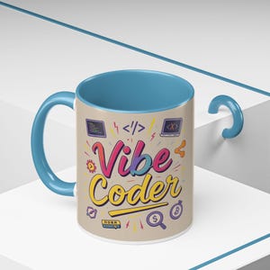 Könnte beinhalten: Eine beige Keramiktasse mit blauem Innenraum und Henkel. Die Tasse trägt den Text "Vibe Coder" in farbenfroher Schrift sowie Icons zum Thema Programmieren. Die Tasse ist etwa 10 cm hoch.