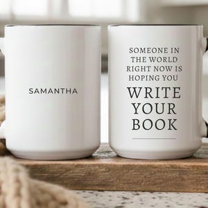 May include: Two white ceramic mugs with black handles and rims. One mug features the name SAMANTHA in black text. The other mug features the black text: SOMEONE IN THE WORLD RIGHT NOW IS HOPING YOU WRITE YOUR BOOK, with a horizontal line below.