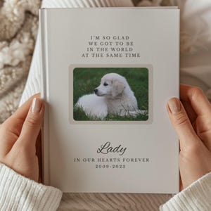 Puede incluir: Un álbum de fotos color crema con una foto de un cachorro blanco en la portada. El álbum tiene el texto "I'M SO GLAD WE GOT TO BE IN THE WORLD AT THE SAME TIME" y "Lady IN OUR HEARTS FOREVER 2009-2023."