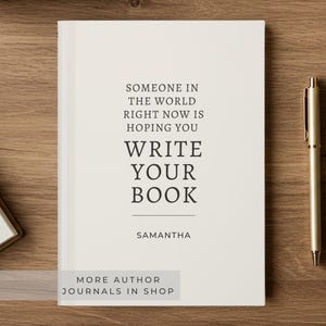 May include: A white journal with black text that reads: SOMEONE IN THE WORLD RIGHT NOW IS HOPING YOU WRITE YOUR BOOK, followed by the name SAMANTHA. A gold pen is positioned to the right of the journal on a wooden surface.