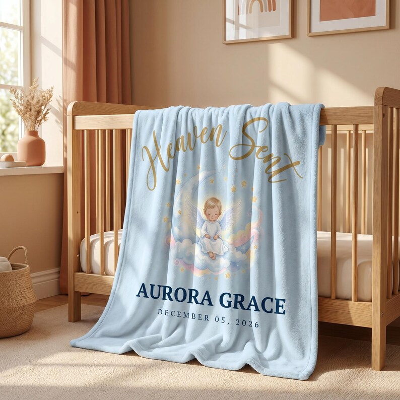 K&ouml;nnte beinhalten: Hellblaue Babydecke mit goldenem Schriftzug "Heaven Sent" und einer Illustration eines Engels auf einem Mond. Die Decke liegt &uuml;ber einem Holzbettchen. Der Name "AURORA GRACE" und das Datum "DECEMBER 05, 2026" sind ebenfalls aufgedruckt.