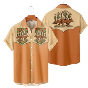 May include: Short-sleeved button-down shirt with a fox and mountain design. The shirt features a tan upper section and sleeves, with a rust-colored lower section. The back of the shirt also has a fox and mountain graphic.