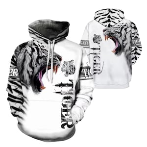 Pode incluir: Um moletom com capuz branco com estampa de tigre em preto e branco, apresentando uma grande cabeça de tigre rugindo na frente e nas costas. A palavra TIGER está impressa verticalmente em letras pretas na frente e horizontalmente nas mangas.