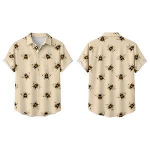 May include: A short-sleeved button-down shirt in a light beige color featuring an all-over print of black and yellow honeybees. The shirt includes a standard collar, a front button placket, and a single chest pocket on the left side of the garment.