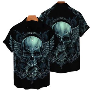 May include: Black button-up shirt featuring a teal skull with feathered wings and chain details. The design is repeated on the back of the shirt. The shirt has short sleeves and a classic collar.