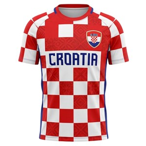 May include: A Croatia soccer jersey with a red and white checkered pattern. The jersey features the word "CROATIA" in blue block letters across the chest, and a Croatian coat of arms emblem. The sleeves and sides have blue accents.