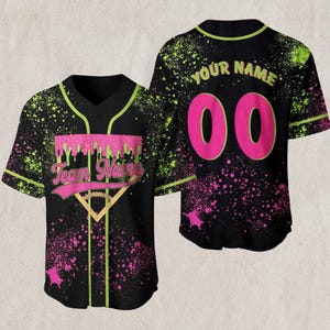 May include: Black baseball jersey with neon green and pink splatter design. The front features a pink banner with the text "Team Name" and a baseball graphic. The back displays "Your Name" above the number "00" in pink.