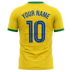 Puede incluir: Camiseta de f&uacute;tbol amarilla con ribetes verdes y el texto "YOUR NAME" sobre el n&uacute;mero "10" en azul. La camiseta tiene un patr&oacute;n sutil y probablemente est&aacute; hecha de una tela transpirable.