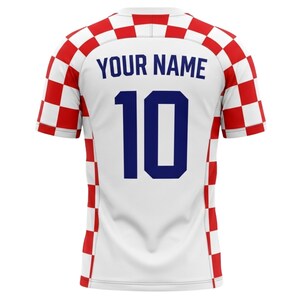 May include: White soccer jersey with red and white checkered accents on the sleeves and shoulders. The back features the number 10 in navy blue and the text "YOUR NAME" above it.