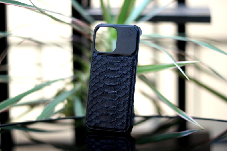 Pode incluir: Capa de telefone preta com um padr&atilde;o texturizado de pele de cobra. A capa tem um recorte retangular para a c&acirc;mera e um acabamento liso e fosco. A capa foi projetada para proteger um smartphone.