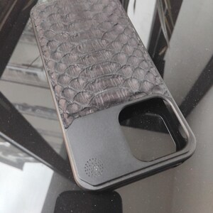 Pode incluir: Uma capa de telefone cinza escuro com um padr&atilde;o texturizado em forma de escamas na parte superior. A parte inferior &eacute; preta fosca s&oacute;lida com recortes para a c&acirc;mera e o alto-falante. A capa tem um design elegante e moderno.