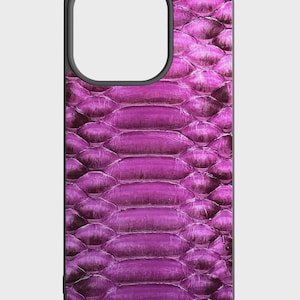 Può includere: Una custodia per telefono con un vivace motivo a pelle di serpente viola. La custodia ha un bordo nero e un ritaglio per la fotocamera. Il design a pelle di serpente presenta un aspetto strutturato, simile a squame, creando un look unico ed elegante. La custodia è progettata per proteggere il telefono aggiungendo un tocco alla moda.