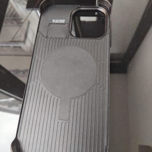 Pode incluir: Capa de telefone preta com uma parte traseira texturizada e uma &aacute;rea de carregamento magn&eacute;tico circular. A capa tem uma borda elevada ao redor da c&acirc;mera e o texto "JIN YU HONG 14-PRO-MAX".