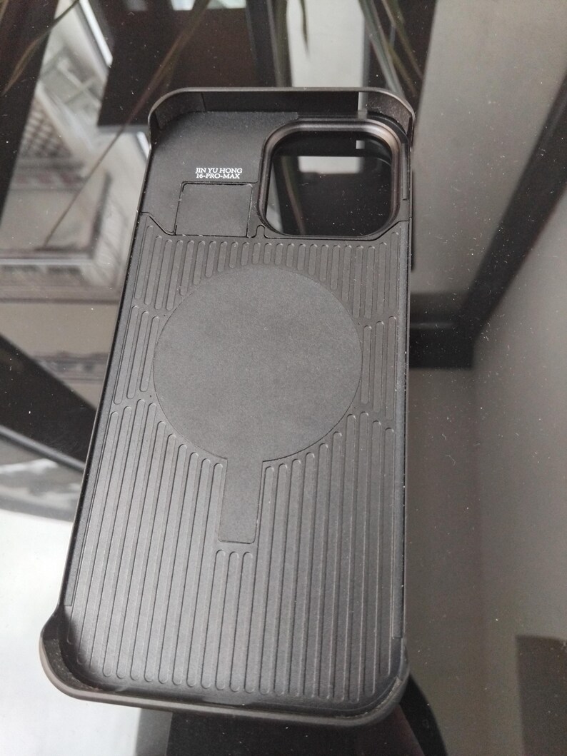 Pode incluir: Capa de telefone preta com uma parte traseira texturizada e uma &aacute;rea de carregamento magn&eacute;tico circular. A capa tem uma borda elevada ao redor da c&acirc;mera e o texto "JIN YU HONG 14-PRO-MAX".