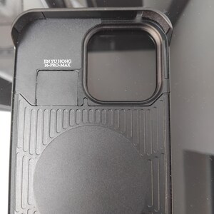 Pode incluir: Capa de telefone preta com uma parte traseira texturizada e um design circular. A capa tem um recorte retangular para a c&acirc;mera e o texto "JIN YU HONG 16-PRO-MAX" impresso na lateral.