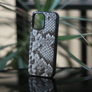 May include: A black phone case with a snakeskin pattern in shades of gray and white. The case has a sleek design and a cutout for the camera. The phone case is designed to protect the phone from scratches and damage.