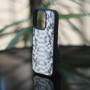 May include: A black phone case with a white and gray snakeskin pattern. The case has a black border and a cutout for the camera. The phone case is standing upright.