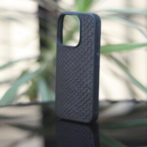 May include: Black phone case with a textured, scale-like pattern. The case has a cutout for the camera and buttons. The case is made of a durable material and provides protection for the phone.