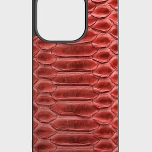 May include: A red snakeskin-textured phone case with a black border. The case has a cutout for the camera and other phone features. The snakeskin pattern is detailed and covers the entire back of the case.