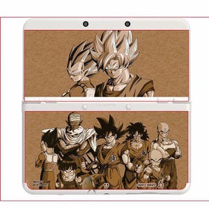 May include: White Nintendo 3DS handheld game console with a brown illustration of Dragon Ball Z characters. The top screen shows Goku and Vegeta, the bottom screen displays a group of characters. The console has two cameras.