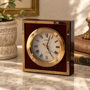Peut inclure: Une horloge à quartz Citizen carrée dotée d'un cadre en bois foncé avec une lunette circulaire en laiton. Le cadran blanc affiche des chiffres romains noirs, de fines aiguilles noires et la marque Citizen imprimée au centre du cadran.