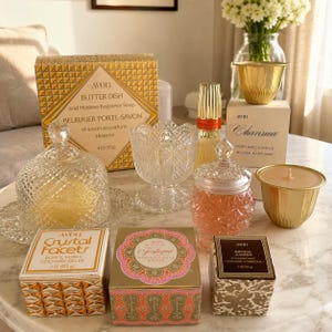 May include: A collection of Avon products including a glass butter dish with lid, a crystal-patterned glass jar, a gold-toned candle, a tall perfume bottle, and several boxed items labelled Crystal Facets, Charisma, and Imperial Garden.