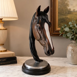 May include: A brown horse head sculpture with a prominent white blaze on its face and a dark mane. The sculpture is mounted on a circular silver-toned metal base, which is attached to a solid black circular pedestal stand for display purposes.