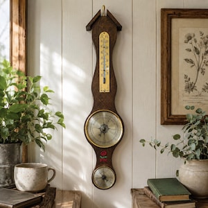 May include: A wall-mounted dark wood weather station featuring a vertical thermometer with C and F scales, a large circular barometer with a gold-toned face labeled Rain, Change, and Fair, and a smaller circular hygrometer below with a red rose graphic.