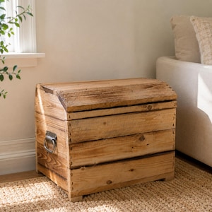 May include: A rectangular wooden chest with a curved lid, constructed from light brown planks with visible wood grain. The storage box features a metal ring handle on the side and is assembled with visible joinery, showcasing a natural finish.