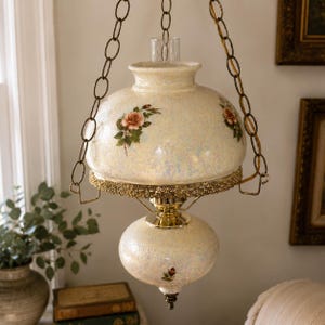 Peut inclure: Une lampe suspendue composée de deux globes en verre crème irisé ornés de motifs de roses. Le luminaire comprend une chaîne en métal doré, une bande en filigrane décorative et une cheminée en verre transparent, suspendue par des fixations.