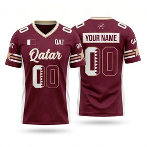 Op de afbeelding: Bordeauxrood en wit sportshirt met het woord "Qatar" in witte letters. Het shirt heeft het nummer "00" in wit met een gouden rand. De achterkant van het shirt heeft de tekst "YOUR NAME" boven het nummer "00".
