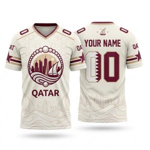 Op de afbeelding: Cr&egrave;mekleurig shirt met bordeauxrode en gouden accenten. Voorzien van een skyline- en zeilbootafbeelding met het woord "QATAR". De achterkant toont "YOUR NAME" boven een bordeauxrood nummer "00".