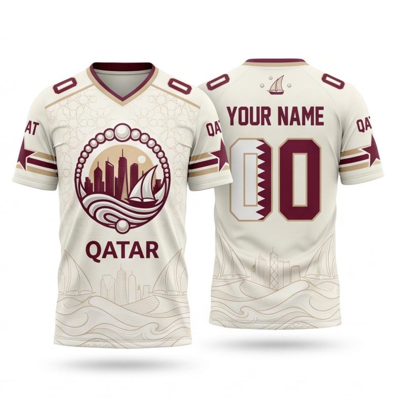 Op de afbeelding: Cr&egrave;mekleurig shirt met bordeauxrode en gouden accenten. Voorzien van een skyline- en zeilbootafbeelding met het woord "QATAR". De achterkant toont "YOUR NAME" boven een bordeauxrood nummer "00".