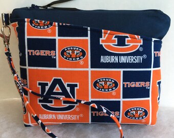 Puede incluir: Una bolsa con cremallera azul y naranja con una correa blanca. La bolsa está hecha de tela con un patrón repetido del logotipo de la Universidad de Auburn, las palabras "Auburn University" y las palabras "Tigers".
