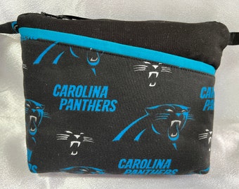 Puede incluir: Bolsa negra con cremallera con un patrón de logotipo de Carolina Panthers. La bolsa tiene un ribete azul y una cremallera.