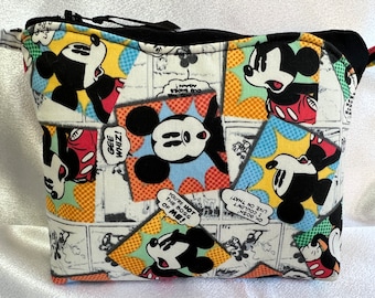 Puede incluir: Una bolsa blanca con cremallera, con una cremallera negra y un cordón negro. La bolsa está cubierta con un estampado colorido de Mickey Mouse en viñetas de cómics. Las viñetas muestran diferentes poses de Mickey Mouse y bocadillos con texto como "Gee Whiz!" y "You're not the boss of me!"