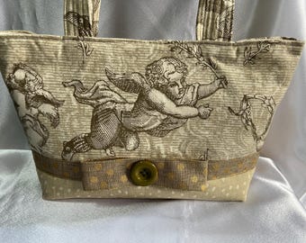 Puede incluir: Una bolsa de tela beige con un diseño de querubín marrón y blanco. La bolsa tiene un botón dorado y una cinta dorada.
