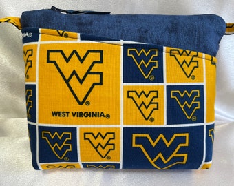 Puede incluir: Una bolsa con cremallera azul y dorada con un patrón repetido del logotipo de la Universidad de Virginia Occidental. La bolsa tiene un forro de tela azul.