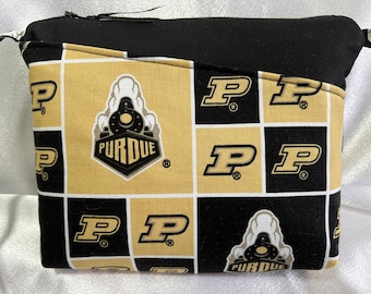Puede incluir: Bolsa de cremallera negra y dorada con un patrón repetido del logotipo de la Universidad Purdue, que incluye una locomotora y la letra 'P'.