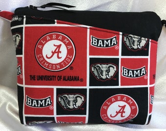 Puede incluir: Una bolsa con cremallera negra y roja con un patrón repetido del logotipo de la Universidad de Alabama, la palabra "BAMA" y una cabeza de elefante. El logotipo es un círculo blanco con una "A" roja y las palabras "Alabama Crimson Tide".