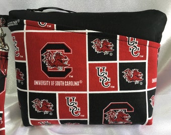 Puede incluir: Bolsa de cremallera negra y roja con un patrón repetido del logotipo de los Gamecocks de la Universidad de Carolina del Sur. La bolsa tiene una cremallera negra y una correa negra.