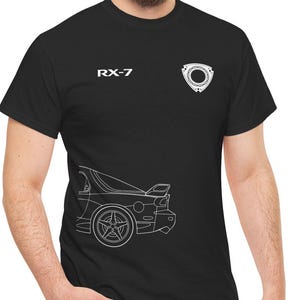 May include: Black t-shirt featuring a white outline of a car and the text "RX-7". The shirt also displays a white rotary engine symbol. The design is printed on a black, short-sleeved t-shirt.
