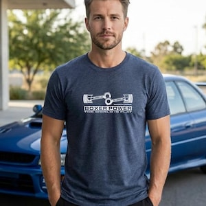 May include: Navy blue t-shirt with a white graphic of engine components and the text "BOXER POWER THE WORLD IS FLAT". A blue car is in the background.
